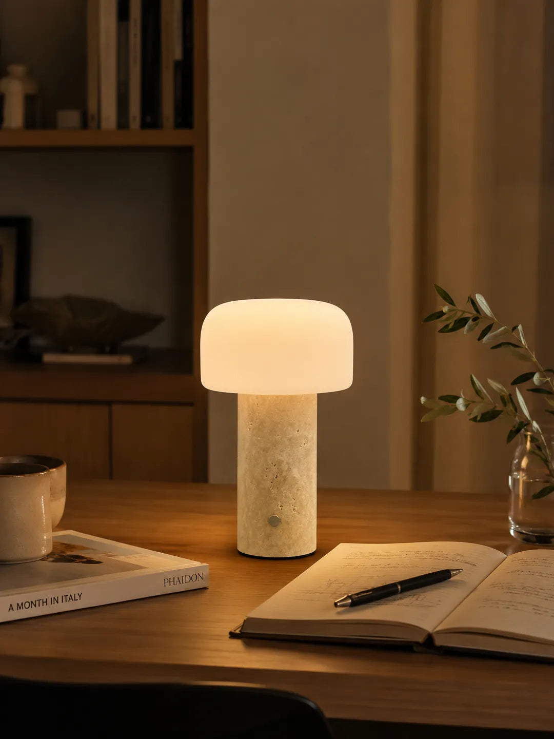 Hooled Vesper Stone Tischleuchte leuchtet auf einem Holztisch neben Notizbuch, Stift und Tasse